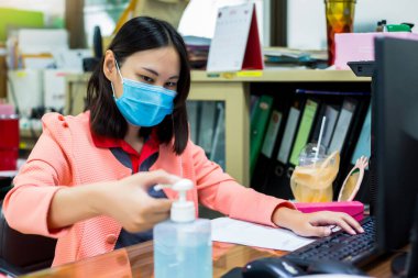 Ofisteki telefon ve bilgisayar klavyesine dokunmadan önce Coronavirus Covid-19 ile kirlenmemek için ellerini alkol dezenfektanıyla yıkayan kadınlara odaklanın. Ofiste temizlik kavramı.