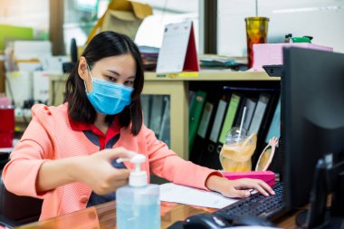 Ofisteki telefon ve bilgisayar klavyesine dokunmadan önce Coronavirus Covid-19 ile kirlenmemek için ellerini alkol dezenfektanıyla yıkayan kadınlara odaklanın. Ofiste temizlik kavramı.