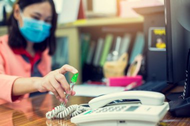 İş kadını, ofiste Coronavirus Covid-19 'a karşı önleyici önlemlere dokunmadan önce alkol spreyli temiz telefon ve bilgisayar klavyesi kullanıyor..