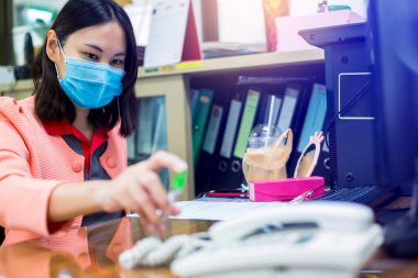 İş kadını, ofiste Coronavirus Covid-19 'a karşı önleyici önlemlere dokunmadan önce alkol spreyli temiz telefon ve bilgisayar klavyesi kullanıyor..