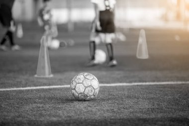 Siyah beyaz arkaplan resmi. Yeşil suni sahada, bulanık futbol takımı eğitimi almış eski bir futbol topu. Futbol akademisinde bulanık çocuk oyunculuk eğitimi ve futbol ekipmanları.