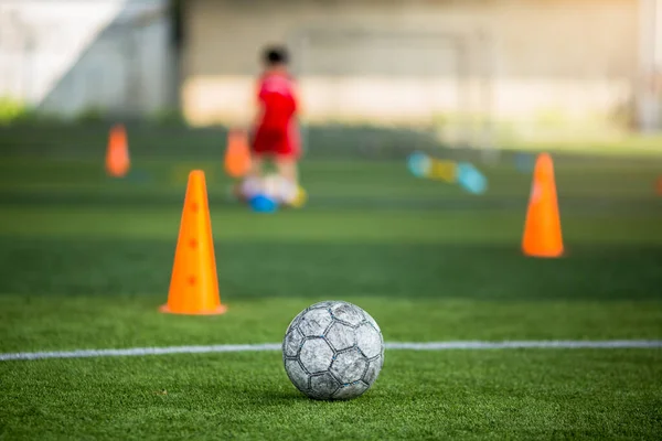 Old soccer ball on green artificial turf with blurry soccer team training. Blurry kid player training and soccer equipment in soccer academy.