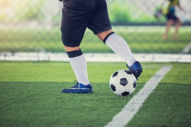 Futbolcu topu yeşil suni sahada atmak için topu kontrol ediyor. Erkek futbolcu maç için antrenman yapıyor. Futbol akademisinde futbolcu..