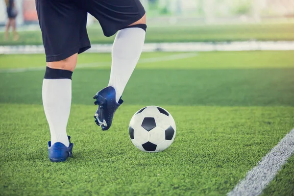Futbolcu topu yeşil suni sahada atmak için topu kontrol ediyor. Erkek futbolcu maç için antrenman yapıyor. Futbol akademisinde futbolcu..