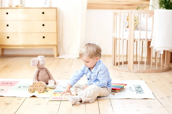 少年は家で木のおもちゃで遊ぶ 子供のための教育用木製のおもちゃ 北欧風の子供部屋の床に座っている少年の肖像画 エコおもちゃ 子供部屋の装飾 — ストック写真