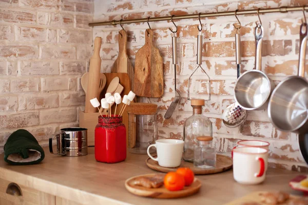 Mutfak düzenleme konsepti. Tavan arası yemek odası tasarımı ve kırsal mutfak. Rafları kancalı tuğla duvar, tahta kesme tahtaları, bankalar, bardaklar. Ev yemeklerinin modern tezgahında mutfak gereçleri.