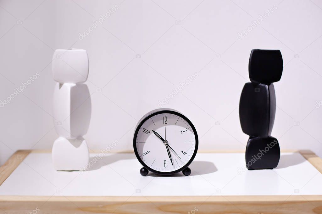 Morning time background, alarm clock near bed at home. Classic alarm clock and two vases in black and white. Front view desk with round black clock with an ceramic vase on white background. minimalism