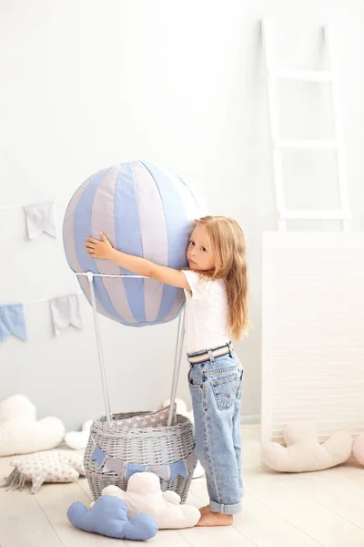 カジュアルな服を着た小さな美しい女の子は 装飾的な風船の背景に立っています 子供は子供部屋で遊ぶ 子供の頃 旅行の概念 誕生日や休日の装飾インテリア — ストック写真