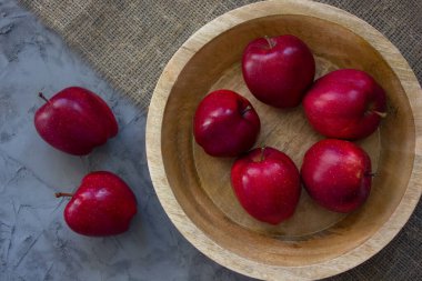 Kırmızı sulu elmalar. Tahta kutuda olgun elmalar. Elmalar tahta tabakta, gri beton masada. Organik gıda, sağlıklı gıda konsepti. Üst Manzara. Koyu taş masada, tahta tepside kırmızı elmalar. Taşralı. Meyve.