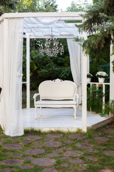 In the garden there is terrace on which a white sofa in style of Provence or rustic. Beautiful sofa is on podium Outdoor. Summer gazebo with white curtains. Wedding decorations. Romantic alcove.