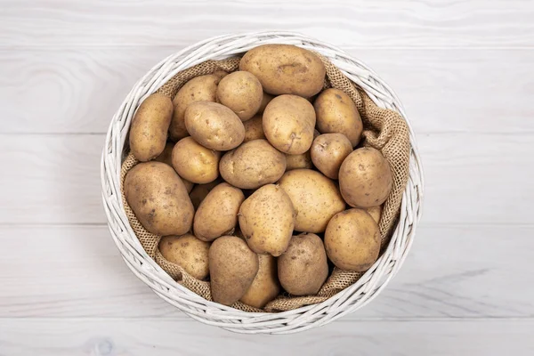 Raw potatoes on rustic basket on white background. Top view — Stock Photo, Image