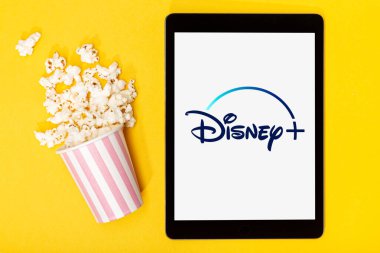 Galiçya, İspanya. 9 Mart 2020, patlamış mısır kovası ve Disney tableti artı sarı arka planda logo. Üst görünüm