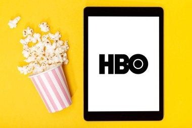 Galiçya, İspanya. 9 Mart 2020, patlamış mısır kovası ve sarı zemin üzerinde HBO logosu olan tablet. Üst görünüm