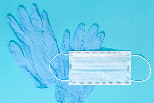 Medical face mask and protective gloves isolated on blue background. Coronavirus COVID-19 protection concept. Copy space. Top view