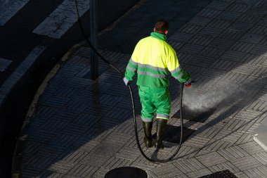 Elinde hortumla kaldırımı suyla temizleyen bir işçi. Kentsel Bakım veya Temizlik Konsepti