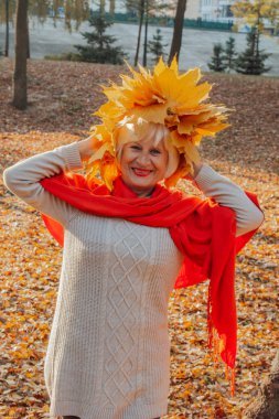 Sevimli yaşlı kadın büyük sarı akçaağaç tutan kafasındaki yaprakların bir çelenk ile yaprakları.