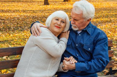 Sonbahar günü bir bankta oturan mutlu yaşlı adam ve kadın. Park bankında oturan rahat yaşlı çift. Büyükbaba nazikçe büyükanneyi alnından öpüyor..