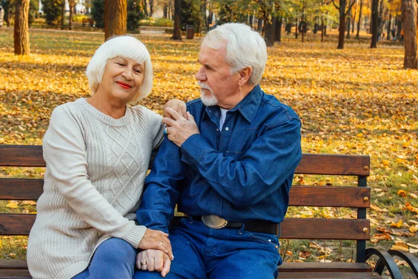 Щасливий літній чоловік і жінка сидять на лавці в осінній день. Розслаблена старша пара сидить на парковій лавці. Дідусь ніжно цілує бабусю на лобі . — стокове фото