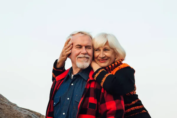 Веселі літні люди жінка і чоловік сидять на камені і обіймаються на озері, на тлі мосту . — стокове фото