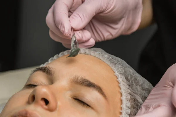 O conceito de cosmetologia. Close-up de uma esteticista aplicando uma máscara verde com uma escova no rosto de uma mulher . — Fotografia de Stock