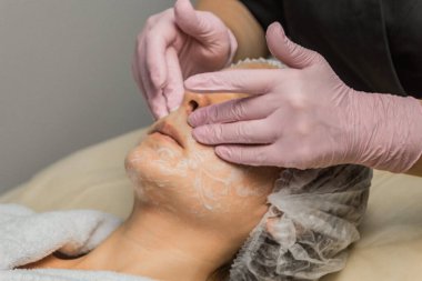 konsept güzellik. Bir kozmetolojistin elleri bir kadının yüzüne krem koyar. Güzellik kızı yüzüne bir krem uygular.