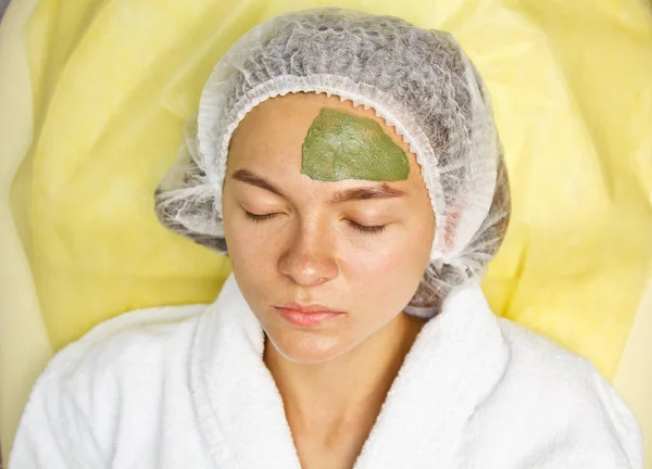Koncept kosmetologie. Detailní záběr kosmetika nanášení zelené masky se štětcem na ženskou tvář. — Stock fotografie