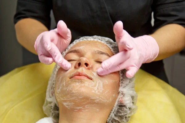 Koncept kosmetolog. Händerna på en kosmetolog sätta grädde på ansiktet av en kvinna. Kosmetolog applicerar en kräm på ansiktet på flickan. — Stockfoto