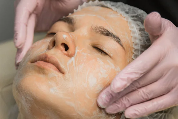 Koncepcja kosmetyczka. Ręce kosmetologa umieścić krem na twarzy kobiety. Kosmetyczka nakłada krem na twarz dziewczyny. — Zdjęcie stockowe