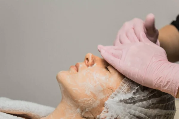 Esteticista conceito. As mãos de um cosmetologist põem a nata na cara de uma mulher. Esteticista aplica um creme no rosto da menina . — Fotografia de Stock