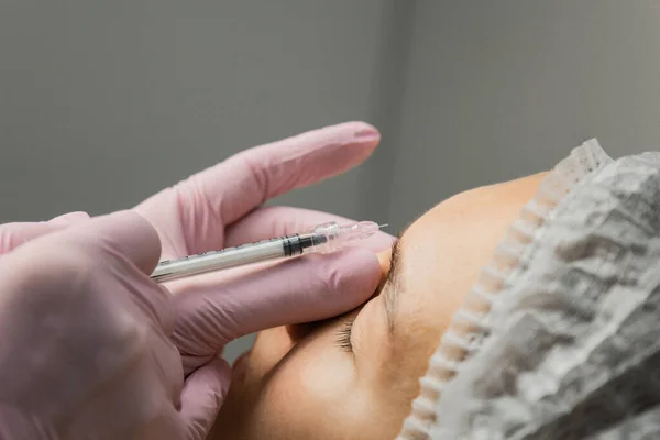 Contorno plástico. Um cosmetologista injeta uma toxina botulínica para apertar e suavizar rugas na pele de uma face feminina. . — Fotografia de Stock