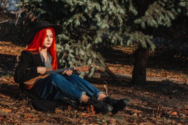 Uzun saçlı seksi kızıl kız ukulele çalıyor. Mükemmel bir kadın portresi. Muhteşem güçlü ve kalın saçlar. Koyu mavi gözler. Doğal güzellik, temiz ten, yüz ve saç bakımı.
