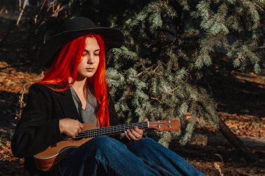 Uzun saçlı seksi kızıl kız ukulele çalıyor. Mükemmel bir kadın portresi. Muhteşem güçlü ve kalın saçlar. Koyu mavi gözler. Doğal güzellik, temiz ten, yüz ve saç bakımı.