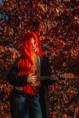 Uzun saçlı seksi kızıl kız ukulele çalıyor. Mükemmel bir kadın portresi. Muhteşem güçlü ve kalın saçlar. Koyu mavi gözler. Doğal güzellik, temiz ten, yüz ve saç bakımı.