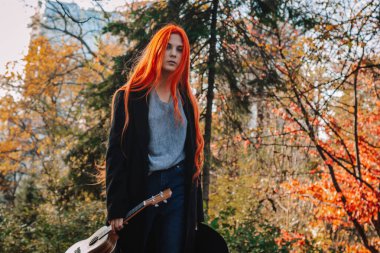 Uzun saçlı seksi kızıl kız ukulele çalıyor. Mükemmel bir kadın portresi. Muhteşem güçlü ve kalın saçlar. Koyu mavi gözler. Doğal güzellik, temiz ten, yüz ve saç bakımı.