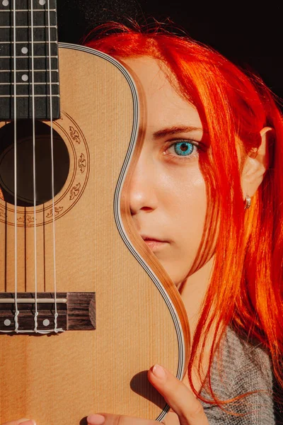 Sexy redhead girl with long hair plays the ukulele. Perfect woman portrait. Gorgeous strong and thick hair. Deep blue eyes. Natural beauty, clean skin, face and hair care.
