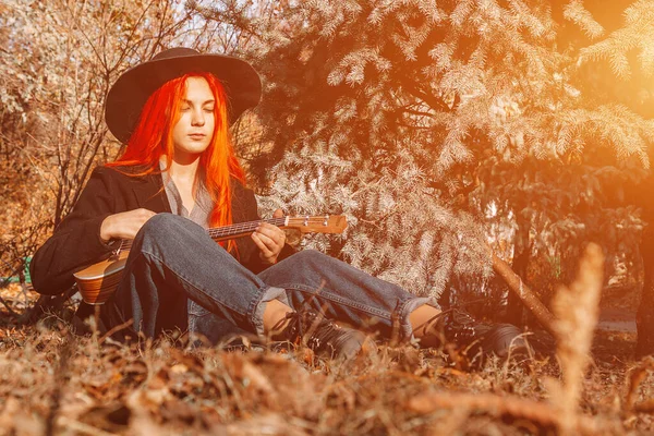 Uzun saçlı seksi kızıl kız ukulele çalıyor. Mükemmel bir kadın portresi. Muhteşem güçlü ve kalın saçlar. Koyu mavi gözler. Doğal güzellik, temiz ten, yüz ve saç bakımı.