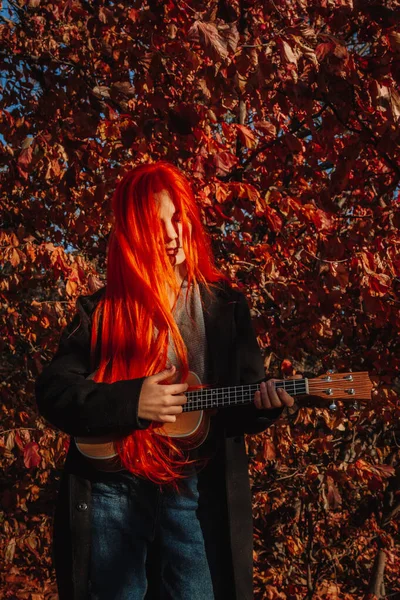 Sexy redhead girl with long hair plays the ukulele. Perfect woman portrait. Gorgeous strong and thick hair. Deep blue eyes. Natural beauty, clean skin, face and hair care.