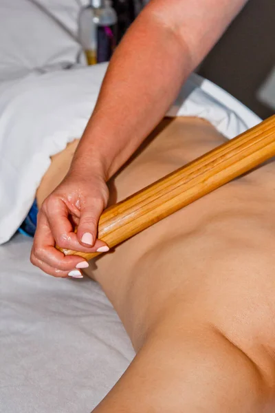 Concepto de bienestar. Masajista profesional le da a un hombre un masaje tailandés con palos de bambú en el spa. Relajación y recuperación después del trabajo . —  Fotos de Stock