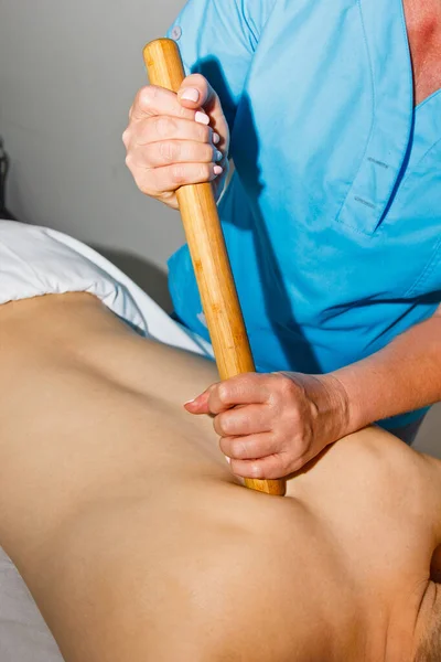 Conceito de bem-estar. massagista profissional dá a um homem uma massagem tailandesa com paus de bambu no spa. Relaxamento e recuperação após o trabalho . — Fotografia de Stock