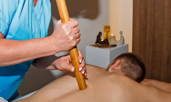 Wellness-Konzept. Ein professioneller Masseur gönnt einem Mann im Wellnessbereich eine Thai-Massage mit Bambusstäben. Entspannung und Erholung nach der Arbeit. — Stockfoto