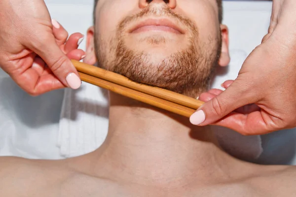 ウェルネスの概念。プロのマッサージ師は、男性にスパセンターで特別な棒を持つタイの顔のマッサージを提供します。仕事後のリラクゼーションと回復. — ストック写真