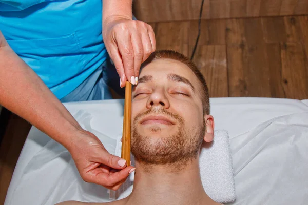 Conceito de bem-estar. Massagista profissional dá a um homem uma massagem facial tailandesa com paus especiais em um centro de spa. Relaxamento e recuperação após o trabalho . — Fotografia de Stock