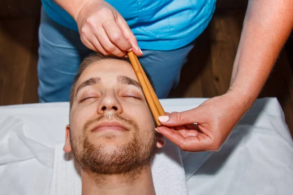 Conceito de bem-estar. Massagista profissional dá a um homem uma massagem facial tailandesa com paus especiais em um centro de spa. Relaxamento e recuperação após o trabalho . — Fotografia de Stock