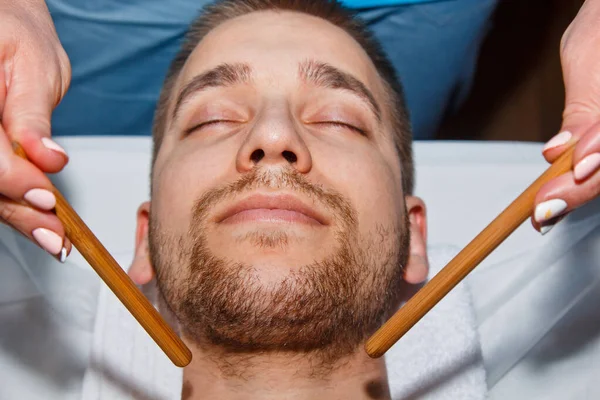 Wellness-Konzept. Ein professioneller Masseur gibt einem Mann in einem Wellness-Center eine thailändische Gesichtsmassage mit speziellen Stöcken. Entspannung und Erholung nach der Arbeit. — Stockfoto