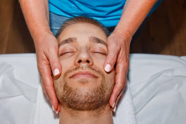 Conceito de bem-estar. Massagista profissional dá a um homem uma massagem facial tailandesa com paus especiais em um centro de spa. Relaxamento e recuperação após o trabalho . — Fotografia de Stock