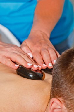 Sağlık konsepti. Lüks bir kaplıca ve sağlık merkezinde geleneksel sıcak taş masajının canlandırıcı etkisi altında rahatlatıcı genç bir adam. İşten sonra iyileşme.