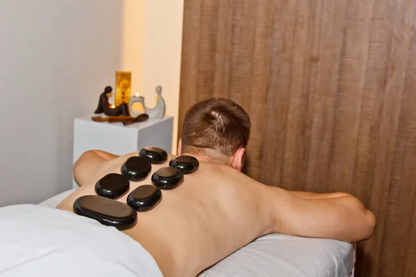 Wellness concept. Handsome young man relaxing under the stimulating effect of a traditional hot stone massage in a luxury spa and wellness center. Recovery after work. — Stock Photo, Image