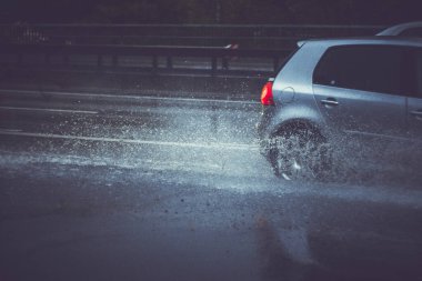 Ukrayna. Kiev - 05,12,2019 Islak şehir asfalt yolunda ilerleyen bir aracın tekerleklerinden su püskürtüyor. Islak bir arabanın tekerleği sular altındaki bir şehir yolunda yağmur altında su birikintisi boyunca hızla hareket eder..