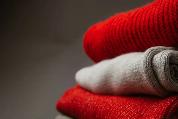 Színes kötött pulóverek mintája közelről. Kézzel készített merino gyapjú termék. Egy halom hajtogatott ruha virágokkal.. — Stock Fotó