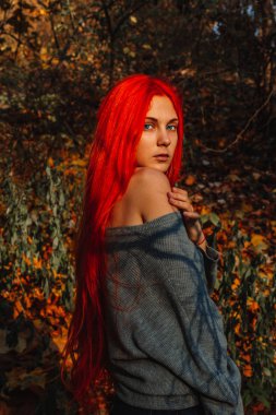 Uzun, güçlü ve kalın saçlı seksi, kızıl saçlı kız. Sonbahar yapraklarının arka planında mükemmel bir kadın portresi. Muhteşem koyu mavi gözler. Doğal güzellik, temiz ten, yüz ve saç bakımı.